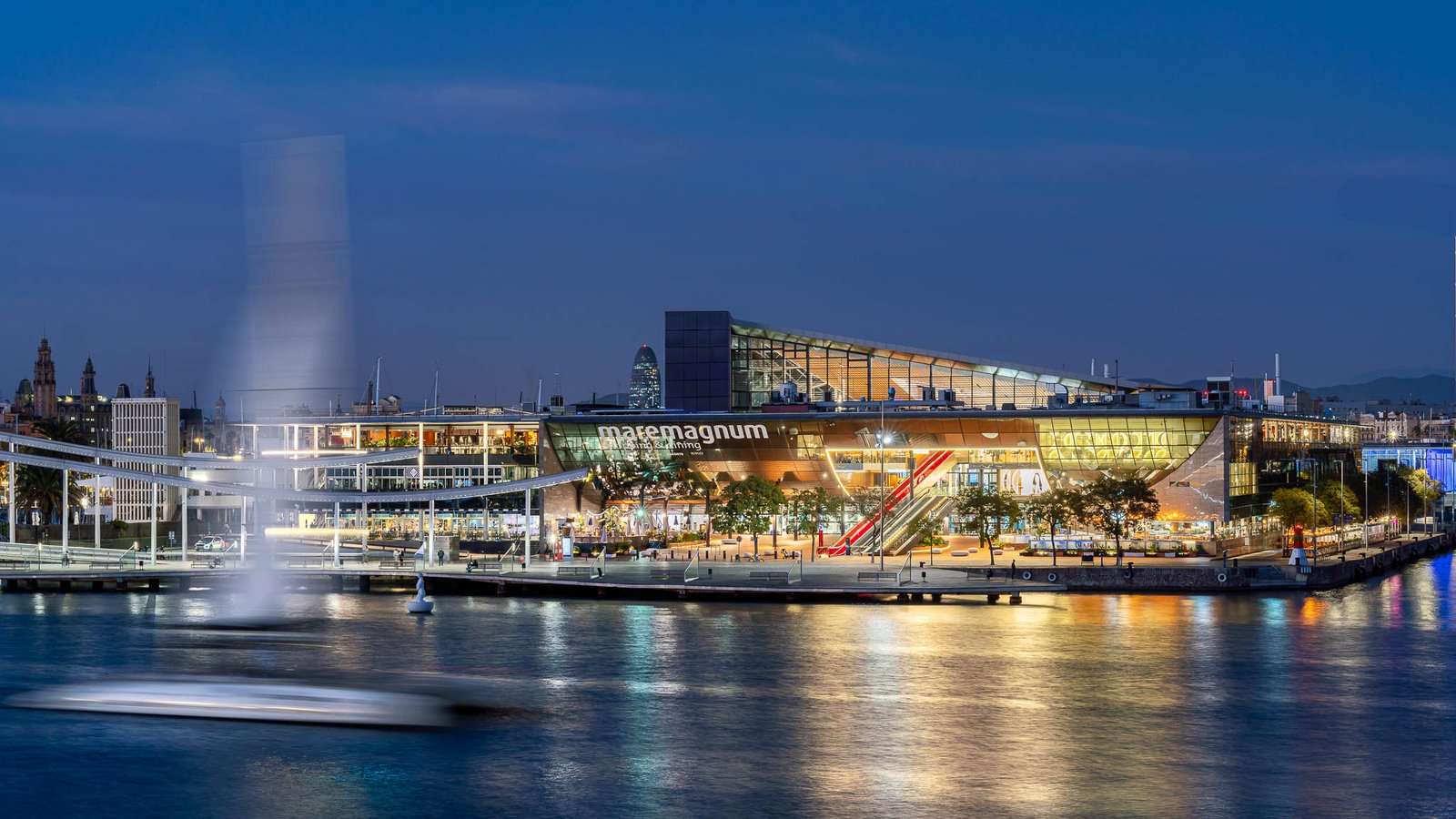 Infographic showing Maremagnum Barcelona 2026 waterfront shopping center in Port Vell with shops, restaurants, opening hours, travel tips, and sunset sea views.